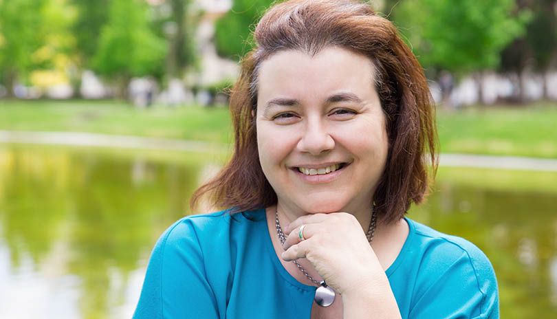 Happy cheerful woman enjoying weekend and leisure time outdoors. Middle aged Caucasian lady in casual standing in park near pond and smiling at camera. Outdoor female portrait concept