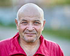 Smirk of balding man in his 60s with stubble on his face.