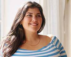 Beauty, bodypositivity, people and lifestyle concept. Indoor shot of gorgeous brunette Latin girl posing by window in kitchen dressed in xxl blue and white striped shirt, having joyful beaming smile
