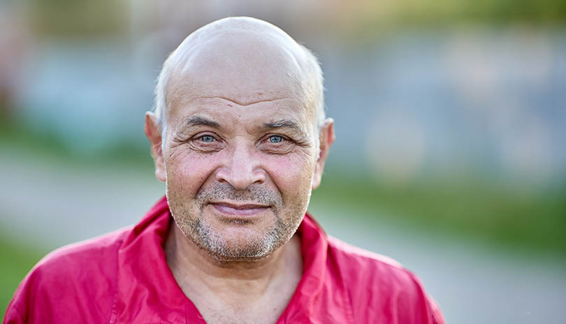 Smirk of balding man in his 60s with stubble on his face.